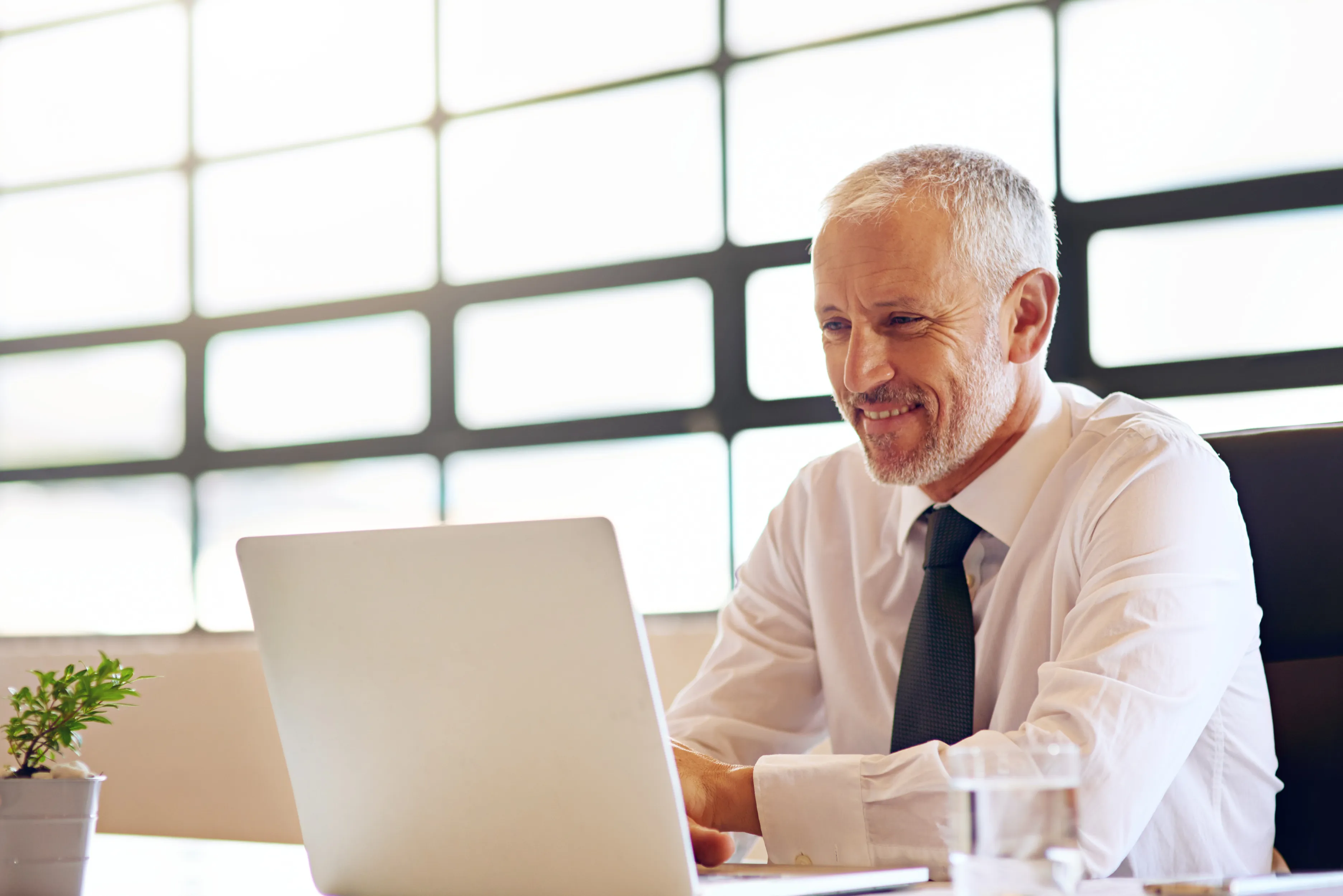 Experienced leadership coach working at a laptop in a bright, window-lined office